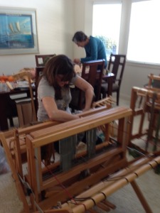 I'm "sleying the reed", which means pulling the warp threads individually through the fixed slots in the reed.  Jen is behind me, working on the warp for her rigid heddle loom.